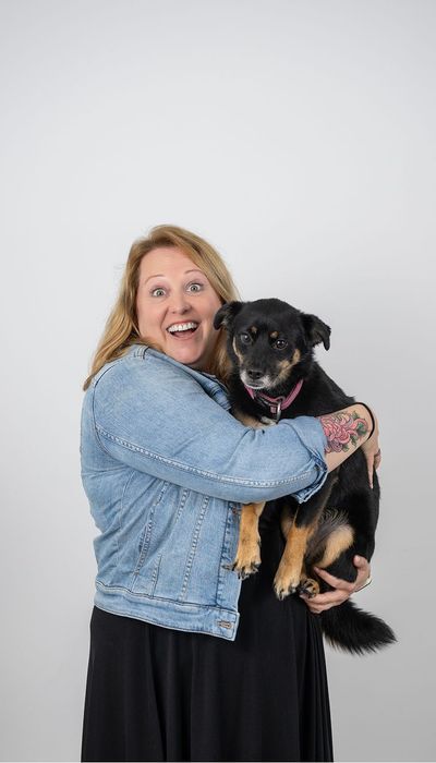 Frau mit lächelndem Ausdruck hält einen kleinen schwarz-braunen Hund im Arm.