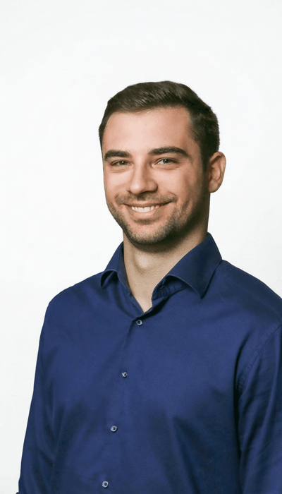 Ein lächelnder Mann in einem blauen Hemd vor einem neutralen Hintergrund.